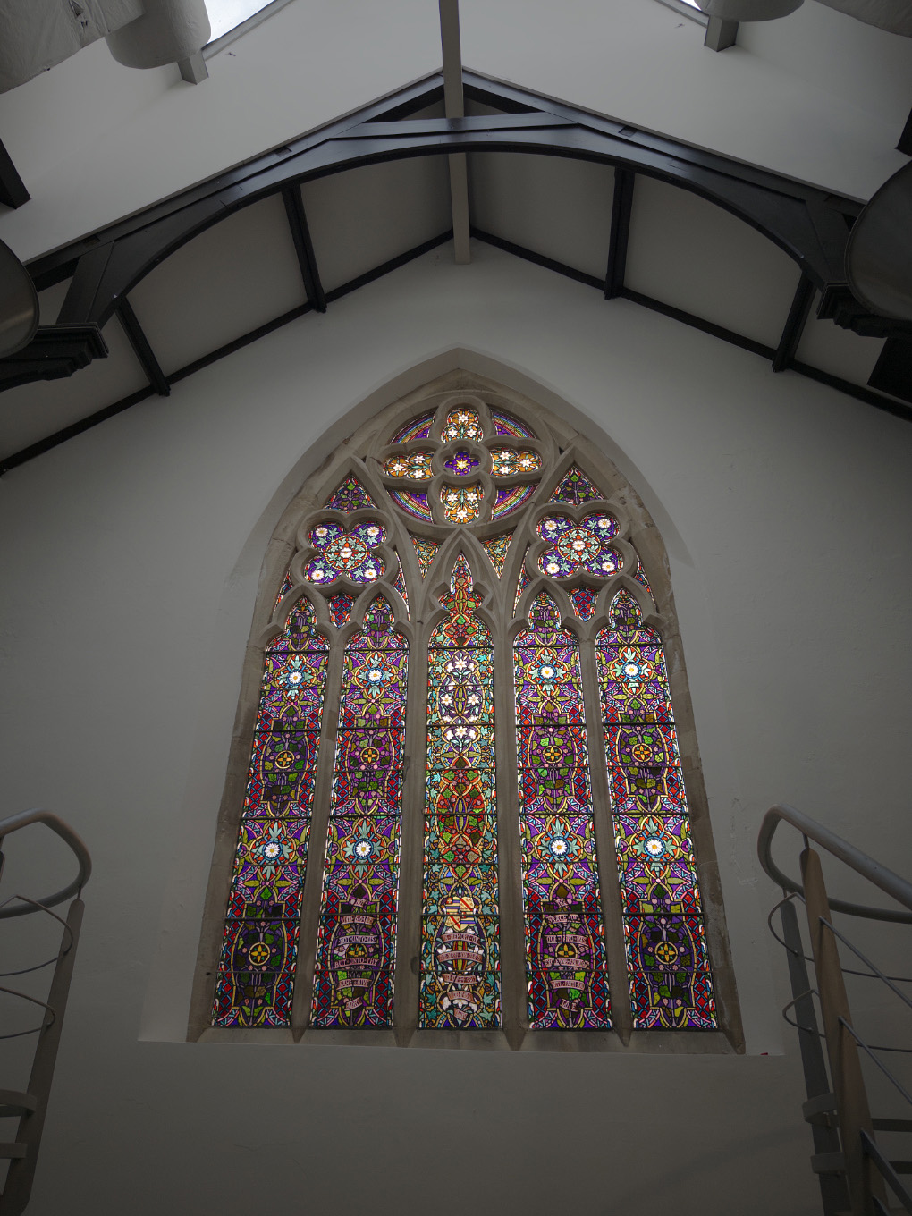 A tall, intricately detailed and highly colourful stained glass window, set into carved stone openings