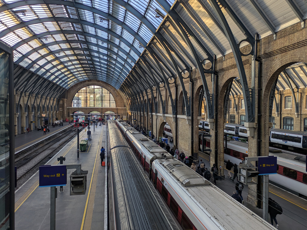 Kings Cross station with it's arched end, arched platform walls, arched ceiling and ironwork viewed from the platform walkway below which intercity trains line the platforms