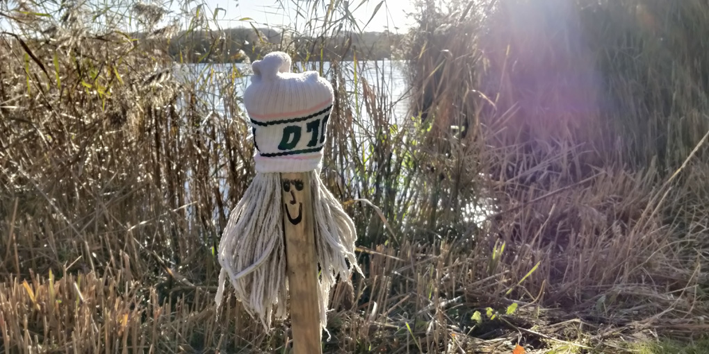 Mop with a face, and a sock for a hat, by a lake. Naturally!