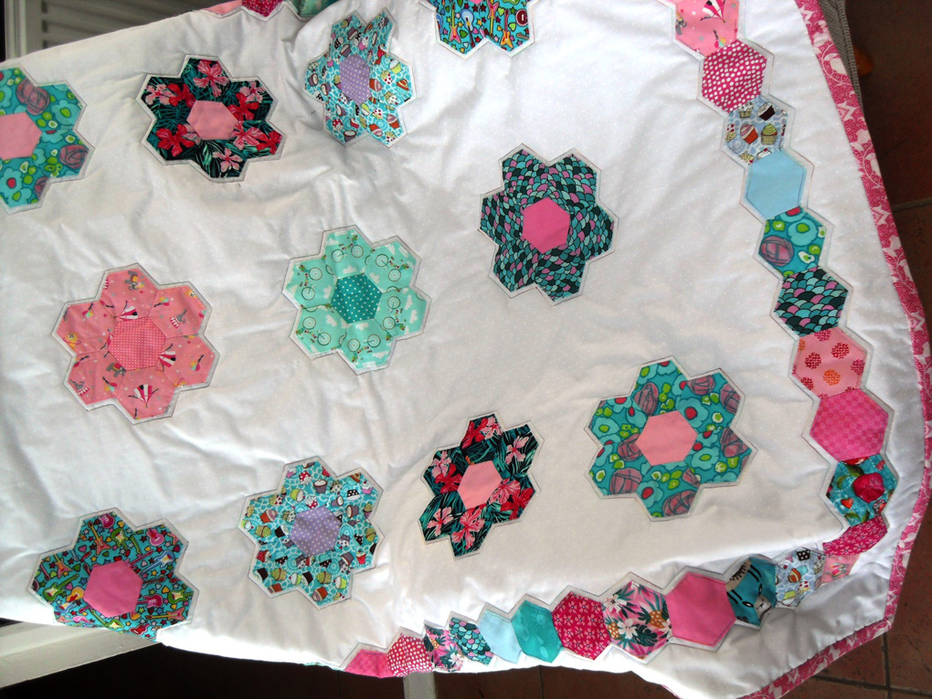 A childs white quilt with multi coloured hexagon flowers