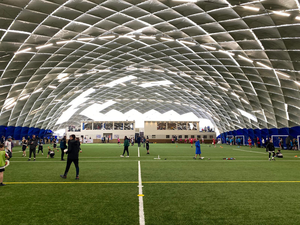 An indoor artificial 3D astro pitch under a white domed roof held up with beams showing in a very geometric pattern.