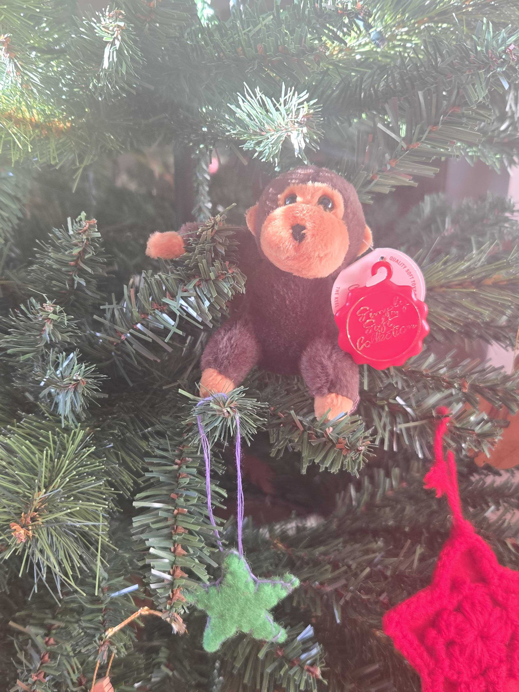A close up of a small brown soft toy monkey is perched on a branch of a Christmas tree