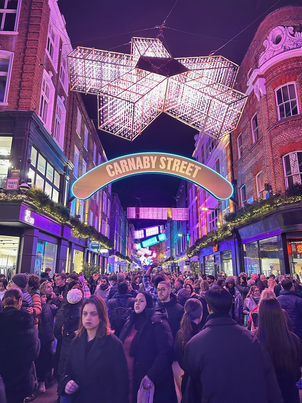 A very busy Carnaby Street in London at Christmas filled with Christmas lights and crowds of people.