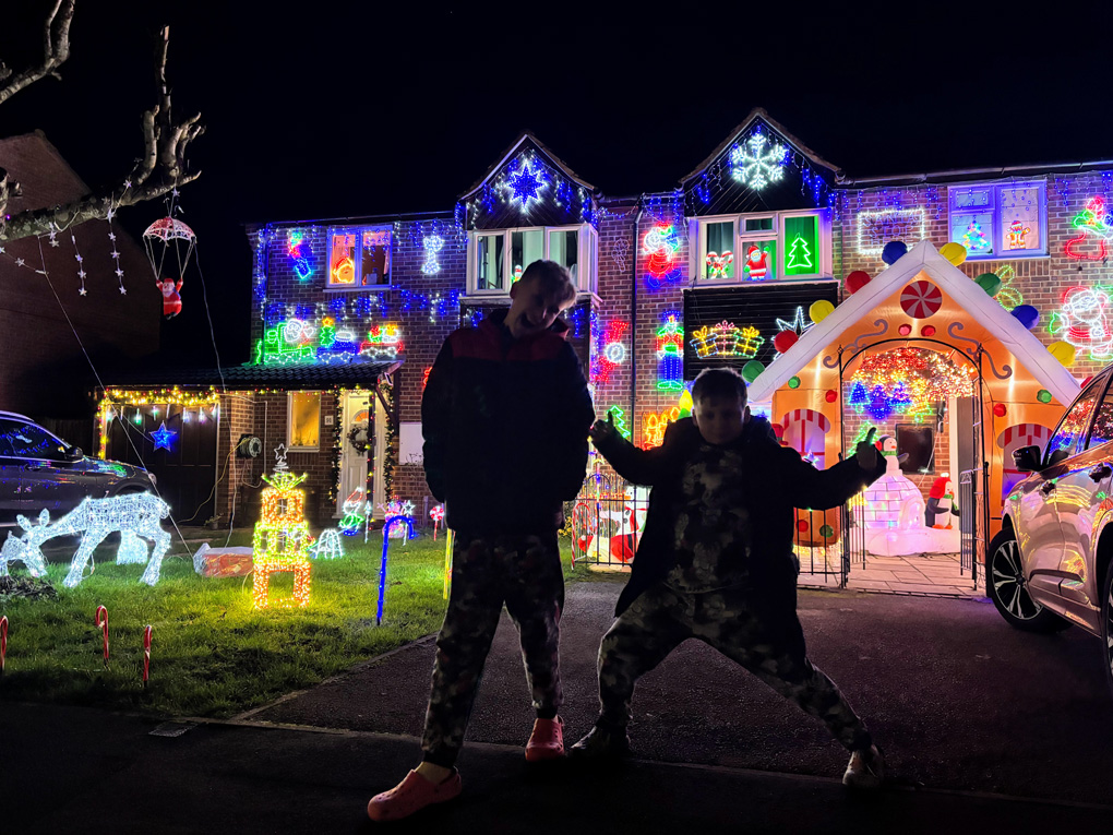My kids standing in front of a colourful house full of lights pulling a funny face and funny pose.