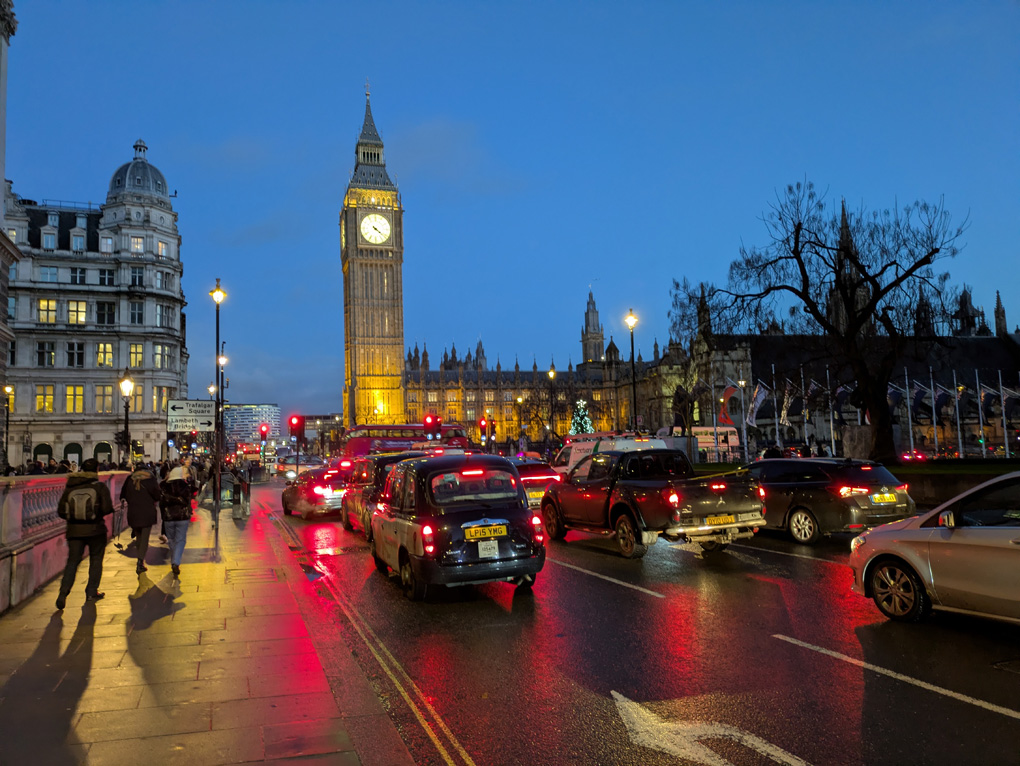 Big Ben with taxis and traffic in the foreground with their red stop lights shining.
