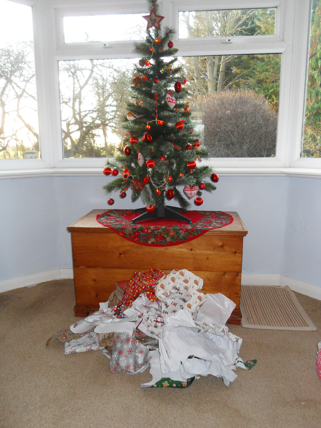 Decorated Xmas tree with heap of discarded wrapping beneath.