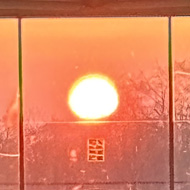 A large red sun is framed at the end of a long corridor. The sunlight has tinted everything red and orange.