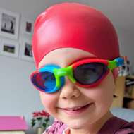Child in multicoloured swimming goggles wearing a swimming cap
