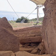 Several large and chiselled limestone rocks show where the outer wall would have been on the temple. A large tent-like canopy is also visible, with the sea in the background.