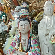 Along concrete steps, hundreds of ceramic models of Buddah and other Gods or religious deities are lined up. Leaves have fallen in amongst the statues, which gives a higgledy-piggledy view stretching up the steps.