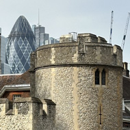 Three turrets of the Tower of London in ascending height from left to right. Gherkin building in distance visible behind and on top of middle turret.
