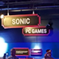 A dark underground room full of video game consoles and computers, sparsely lit by multi-coloured neon lighting