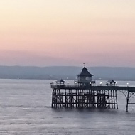 At the end of a great pre Easter stay in Clevedon, Somerset, I managed to capture the peaceful promenade just as the sun had disappeared into the sea. A string of white lights lit up the promenade and some colourful boats lay in wait to be used again. The tide was slowly rolling in over the pebbly beach. At the end of the prom the beautiful unspoilt Victorian pier jutted out like a piece of black picot lace over the sea. The sun had left subtle stripes of pink and blue caressing the horizon. There wasn’t a soul about, all was still. What a lovely sight on my last night there!