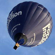 Looking almost directly upwards at a black hot air balloon in a blue sky that is streaked with white clouds. It looks like it is flying up towards the top right corner of the frame.