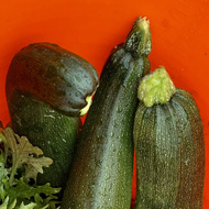 A orange trug with salad leaves and many courgettes