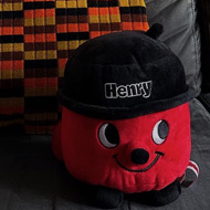 A Henry vacuum cleaner plush toy on a safe with an orange and black moquette cushion behind. A frame print of Pink Floyd's Wish You Were Here on top of sofa.
