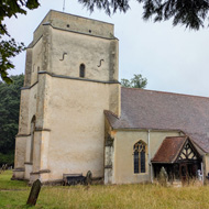 An old square towered church in a wooded churchyard on a rainy day