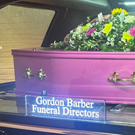 A pink coffin in the back of a hearse