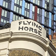 An old London pub in the foreground, juxtaposed with two colourful high-rise blocks in the background.