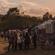Evening sun, festival tents adorned with flags, view across the hills of Bath