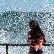 Waves splashing over a teenage girl standing on the side of a harbour on the Atlantic coast