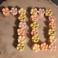 Photo looking directly down on a Victoria sponge cake. It has not fully risen and is not totally circular. The top is covered in pink icing and has small sugar flowers spelling out 70