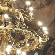 A chandelier in a small but very ornately designed Orthodox Church. The ceiling is painted with saints and religious images. The chandelier looks, at first, like a normal one with candle-shaped lightbulbs, but on closer inspection, the “chains” between the sections are made from bullets and the centre is made from blades, swords and bayonets.