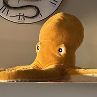 A yellow plush octopus sits atop a white SMEG fridge with a clock above it, showing a snake coiled around the clock face with Roman numerals.