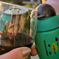 Three hands bringing together a glass of red wine, a can of beer, and a little toddler's cup in a 'cheers' motion