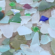 A large pile of sea glass on a concrete barrier by the beach. The glass is mostly frosted whites, greens and browns, with a few blues and reds.
