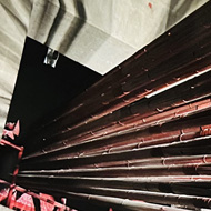 Interior lit concrete room with multiple red steel cables emanating from a square hole. The cables are long and straight, giving of spectral light and reflection their red colouring in the shadows.