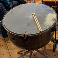 A view from behind two timpani looking out at the rest of the orchestra in a church.