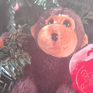 A close up of a small brown soft toy monkey is perched on a branch of a Christmas tree