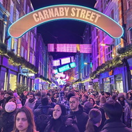 A very busy Carnaby Street in London at Christmas filled with Christmas lights and crowds of people.