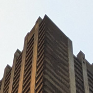 The view from the foot of one of the Barbican Estate towers looking up, its angular concrete floors and balconies disappearing almost to a point with the late low sun catching one side in golden light