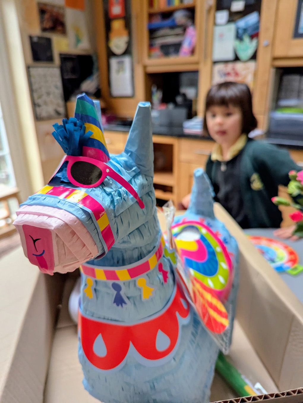 Pinata shaped like a llama wearing sunglasses, with girl in background.
