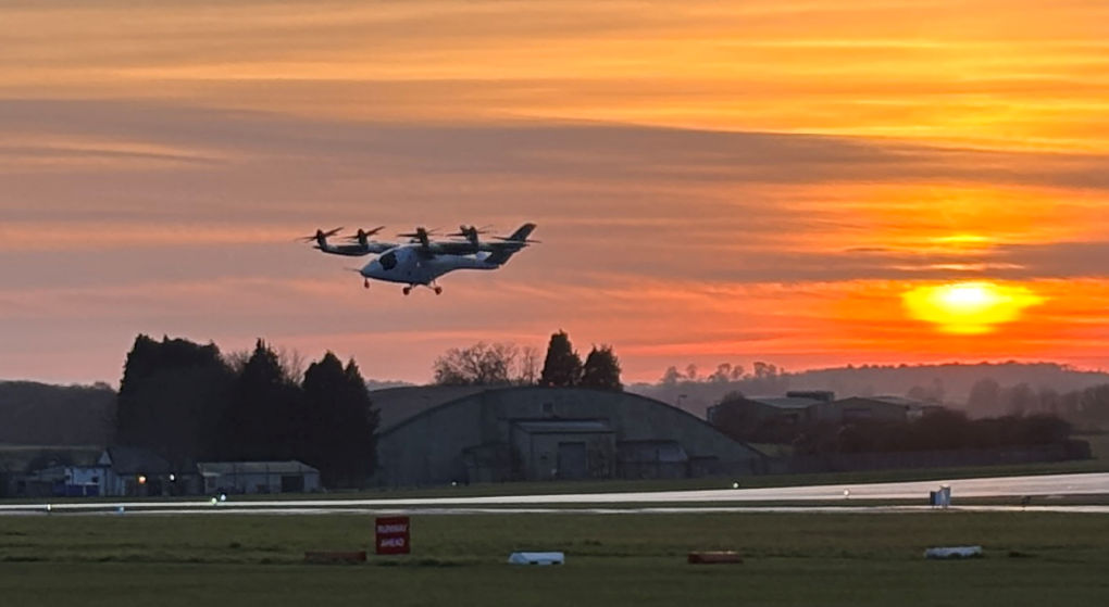 Against a sunset backdrop a four prop, chubby aircraft can be seen maintaining a  fixed height just above the runway.