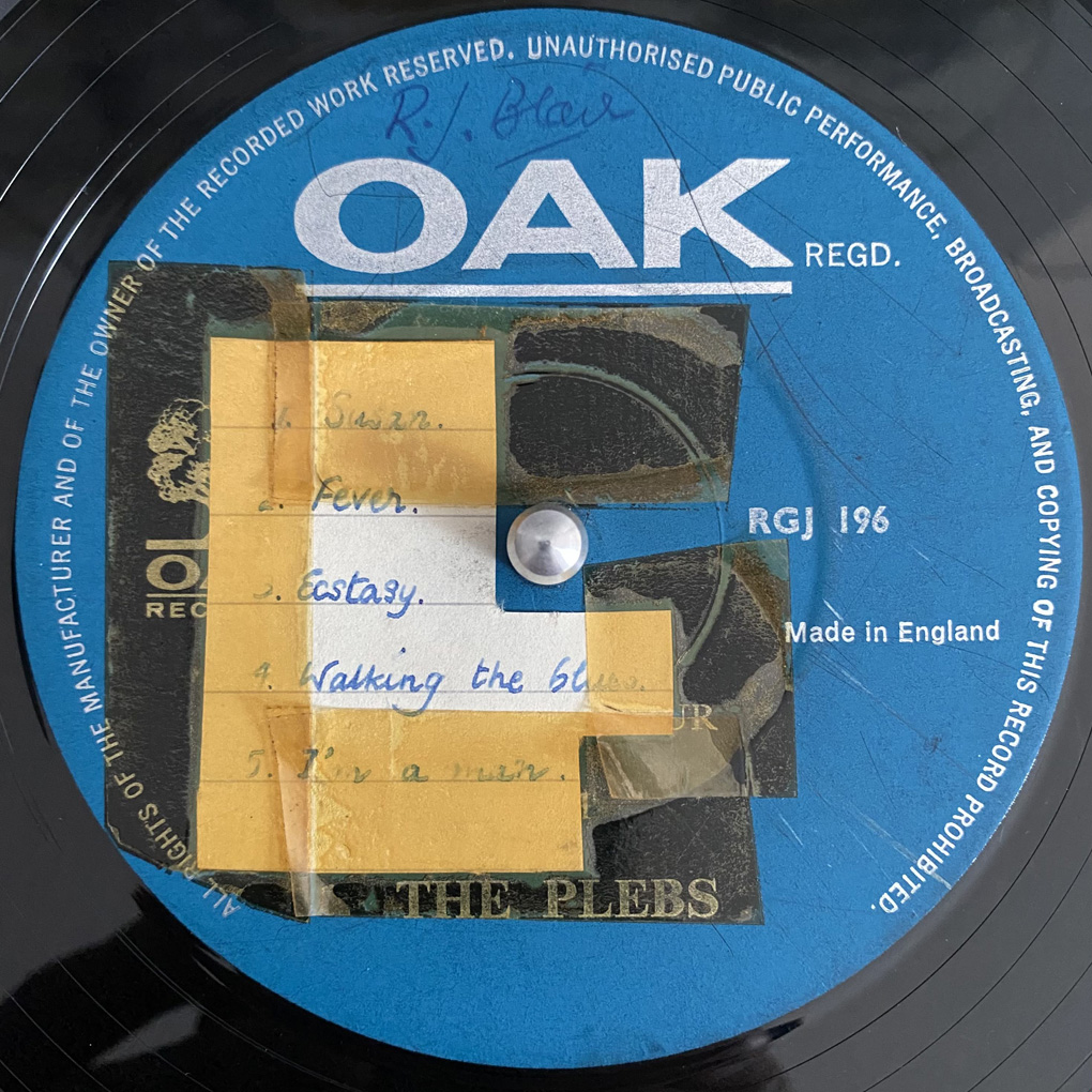 The label of a record, blue, with a hand-written track list attached with yellowed tape, and the band name 