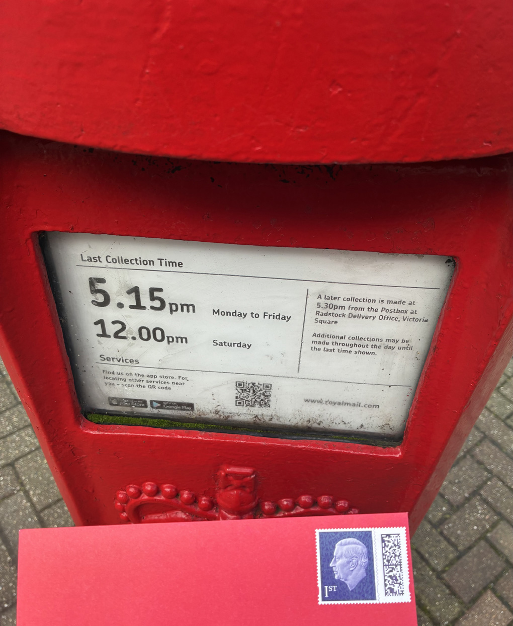 A red envelope with a kings head stamp, about to be placed in a red letter box