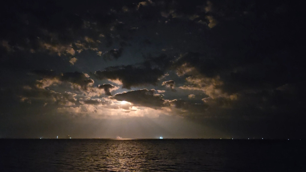 Low cloud over a body of water, bright light emitting from center caused by the burners from a rocket launch