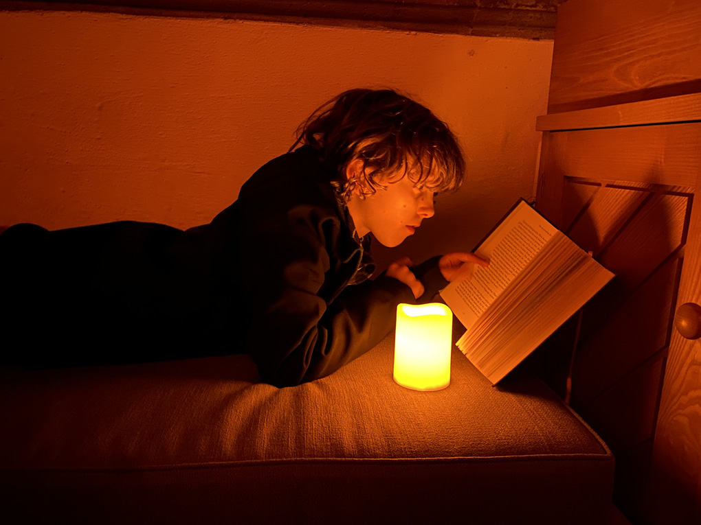 A boy reading a book by candlelight