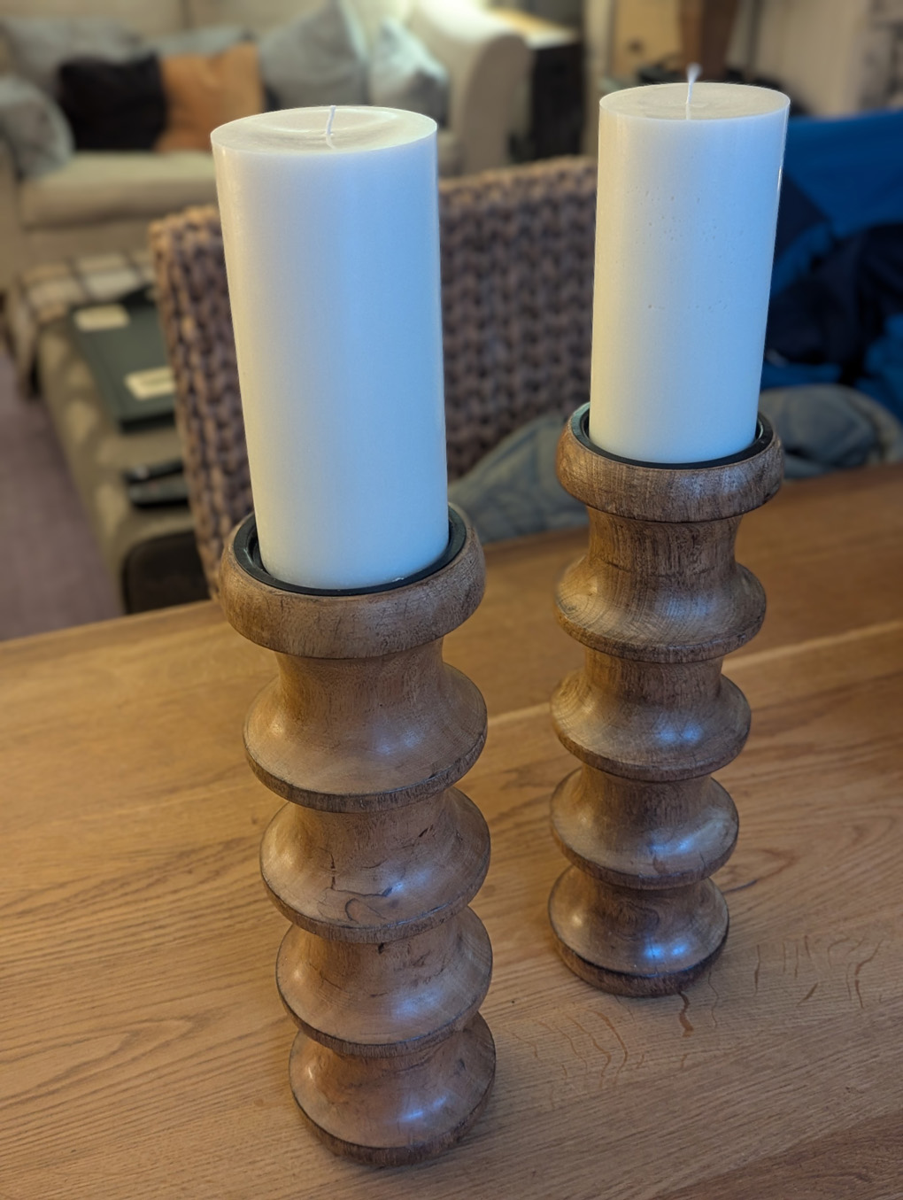 Two wooden candlesticks with round white candles, standing on a wooden table.