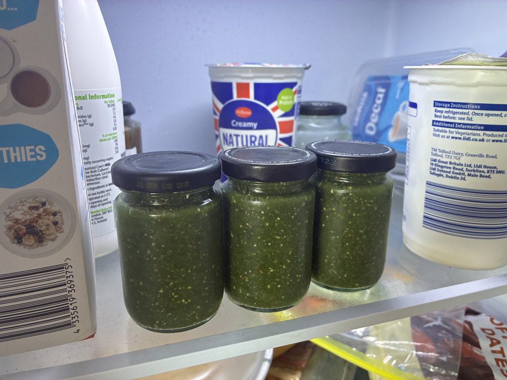 Three little bottles of green puréed food, on a shelf in a fridge.