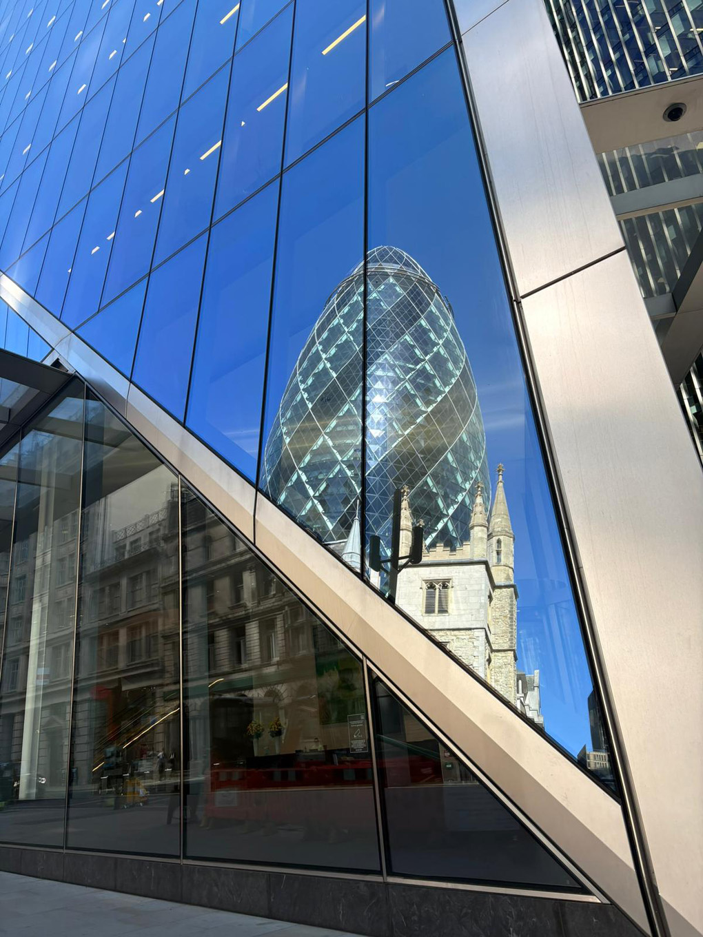 The famous “Gherkin” building and much older stone building reflected in an other glass building. Showing the different eras of London architecture