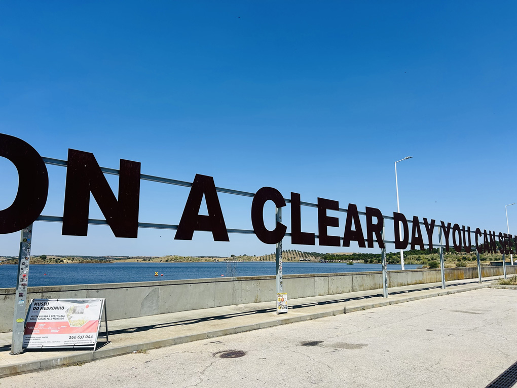 Sunny day in a hot country. On top of a dam is a huge sign in mental reading “on a clear day you can see forever “