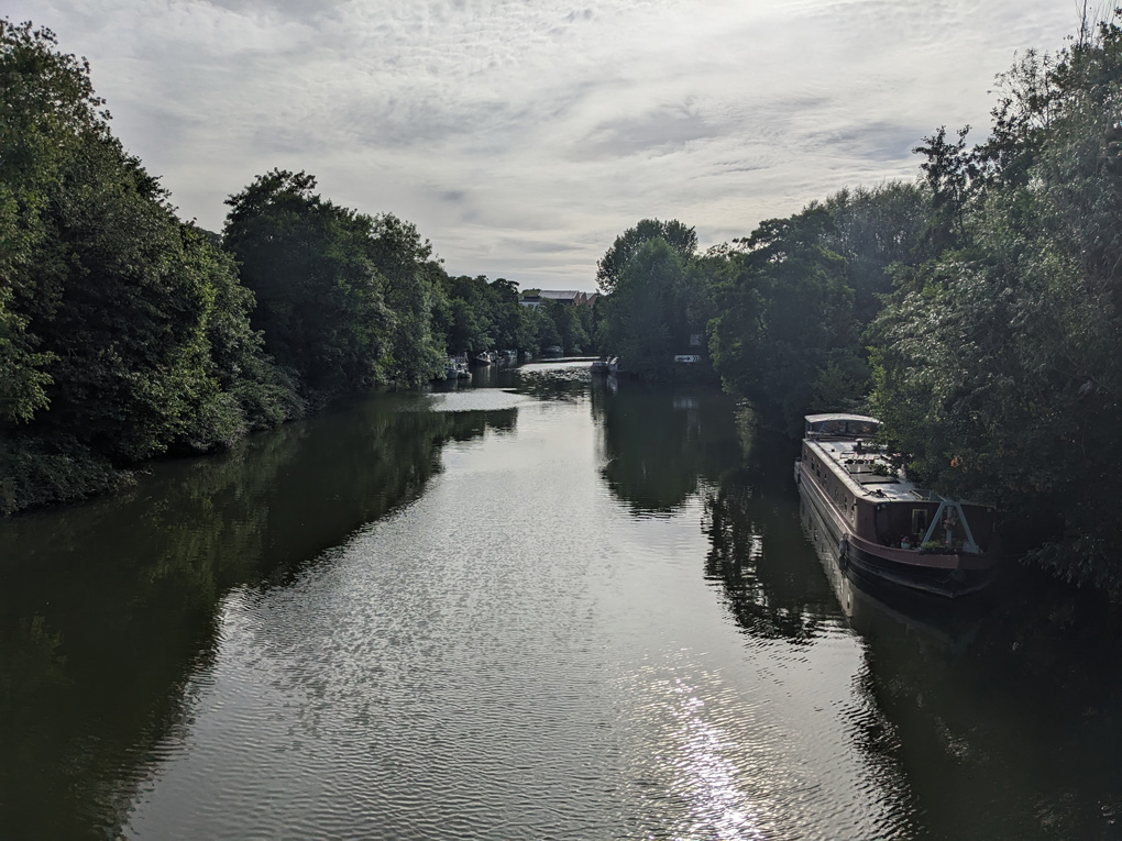 View over the river in the evening sun, a canal boat moored on one side and trees lining the banks
