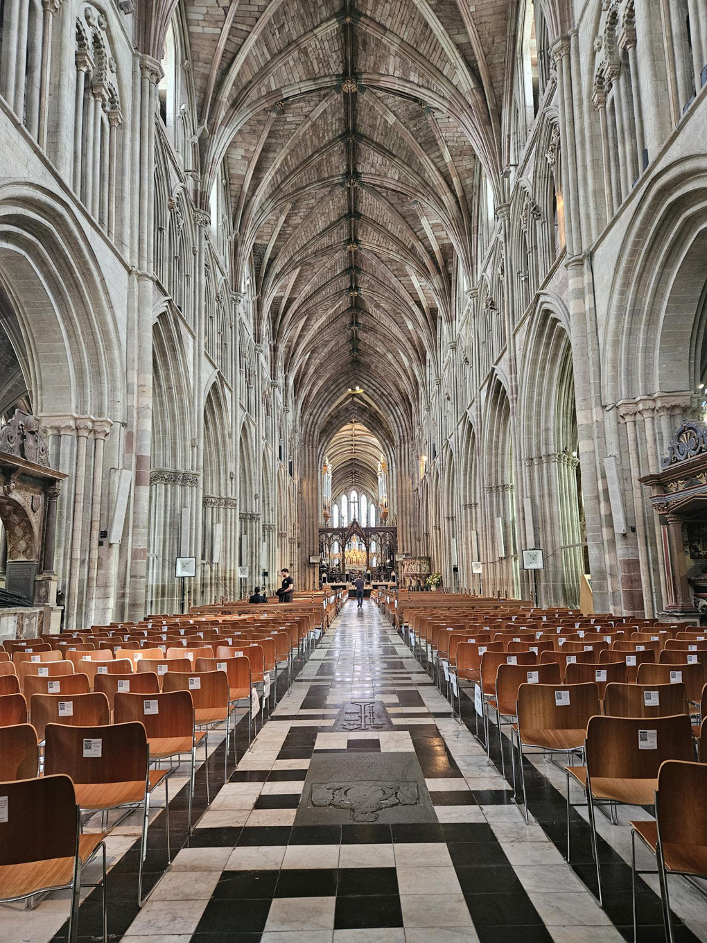 View inside a grand cathedral with soaring stone arches, vaulted ceiling leading to an alter in the distance and rows of wooden chairs