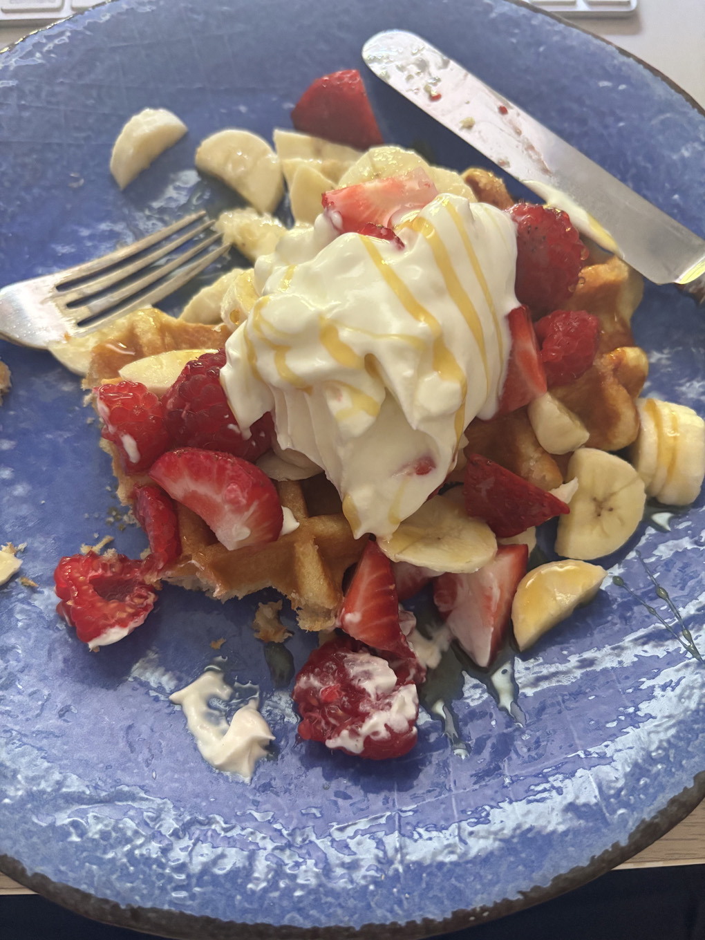 A pile of sugar waffles, fresh fruit, Greek yoghurt and honey on a bright blue plate