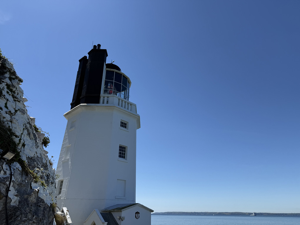A large white lighthouse in the foreground with blue sea and sky in the background