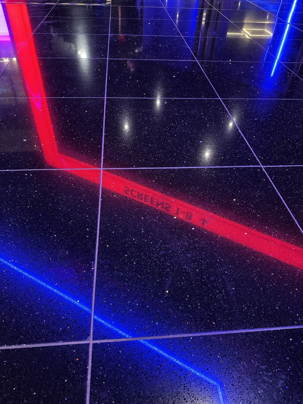 A black reflective floor showing blue and red neon signage in reverse